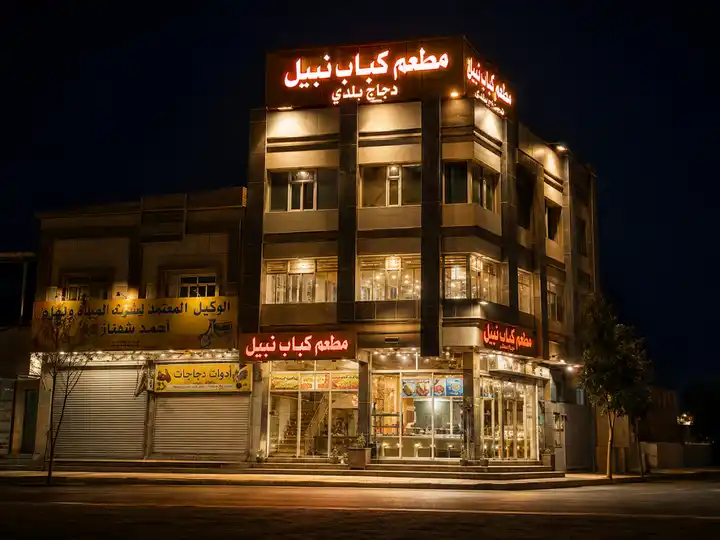 واجهة مطعم كباب نبيل مضاءة ليلًا بلافتات حمراء